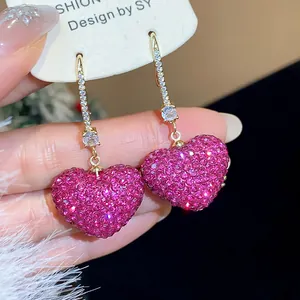 Close-up of pink micro-paved heart earrings with sparkling crystal-accented gold ear hooks