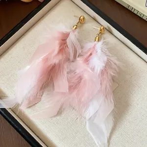 Detailed view of elegant pink and white feather tassel earrings in a cream jewelry box