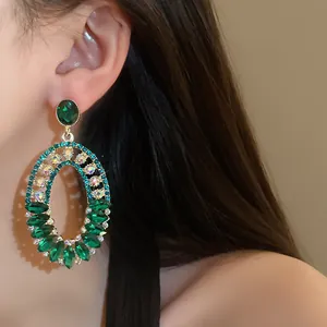 Detailed view of vintage emerald green rhinestone oval dangle earrings worn by a model