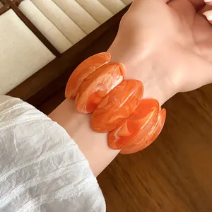 Vista dettagliata di un bracciale ovale in acrilico marmorizzato arancione al polso.