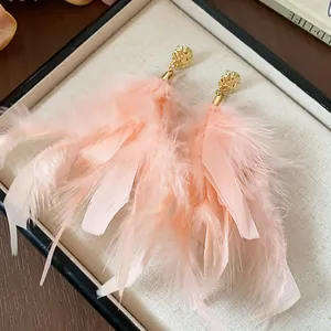 Close-up detail of delicate pink feather tassel earrings with hammered gold studs