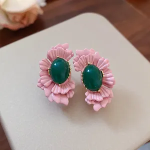 Makro-Detailansicht von rosa Blütenblättern-Ohrringen mit grünen ovalen Glassteinen.