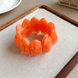 Dettaglio di bracciale in acrilico arancione marmorizzato su espositore beige.