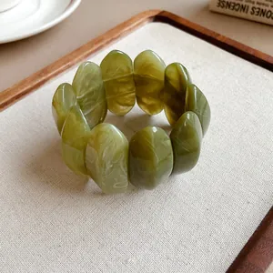 Dettaglio ravvicinato di un bracciale ovale in acrilico verde oliva marmorizzato su vassoio