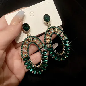 Close-up of vintage emerald rhinestone oval earrings with gold-tone setting and glitter details.