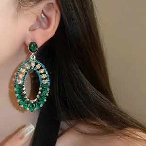 Close-up view of elegant vintage oval drop earrings featuring green marquise crystals on ear.