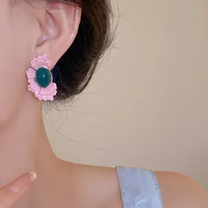 Nahaufnahme von süßen rosa Blumenohrringen mit grünem ovalem Glasstein am Ohr des Models
