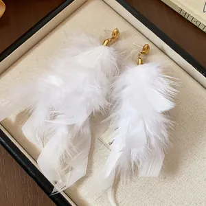 Macro detail of exquisite white feather tassel stud earrings with elegant gold hardware