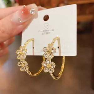 Detailed close-up of gold-plated hoop earrings with rhinestone-studded flower charms