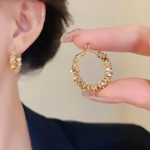 Gros plan de boucles d'oreilles créoles dorées en argent concassé irrégulier tenues par des doigts