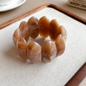 Dettaglio macro di un bracciale in grani di acrilico marmorizzato marrone su vassoio beige