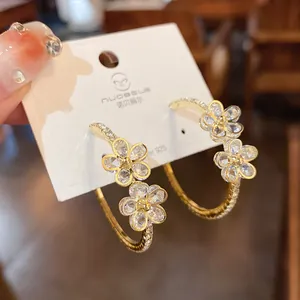 Macro detail of gold-plated hoop earrings with sparkling rhinestone flower charms