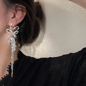 Elegant long sparkling rhinestone bow and heart tassel drop earrings worn by a model