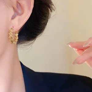 Gros plan de boucles d'oreilles créoles dorées à texture irrégulière portées à l'oreille