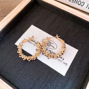 Vue détaillée de boucles d'oreilles créoles dorées avec une texture d'argent concassé.