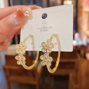 Detailed close-up of elegant gold-plated flower hoop earrings with sparkling rhinestones.
