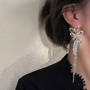 Detailed view of long silver rhinestone heart bow tassel earrings worn by a model