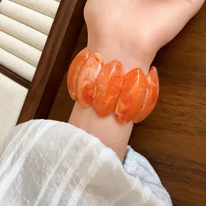 Primo piano di un braccialetto in acrilico marmorizzato arancione con segmenti ovali.