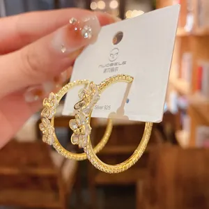 Macro detail of gold-plated hoop earrings featuring elegant crystal flower designs.