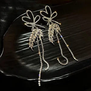 Detailed macro view of elegant rhinestone bow and heart tassel drop earrings on black tray.
