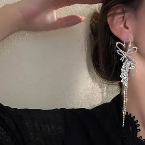 Detailed view of elegant silver bow tassel earrings with sparkling rhinestones on model