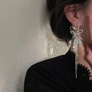 Close-up detail of sparkling diamond-encrusted heart tassel earrings worn by a model