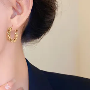 Gros plan de boucles d'oreilles créoles dorées irrégulières avec texture métallique