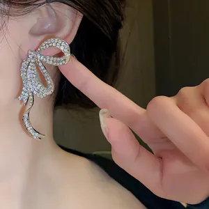 Detailed view of elegant silver rhinestone bow tassel earrings on an Asian model's ear