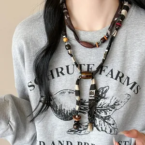 Detail van een boheemse retro stoffen en houten kralenketting op een grijze sweatshirt.