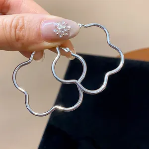 Minimalist silver-plated flower-shaped hoop earrings held by hand to show detail