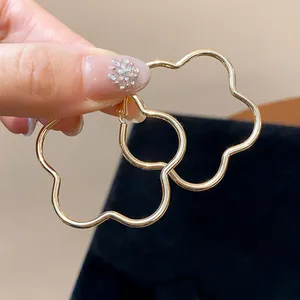 Detailed close-up of elegant gold-toned flower-shaped hoop earrings held by hand