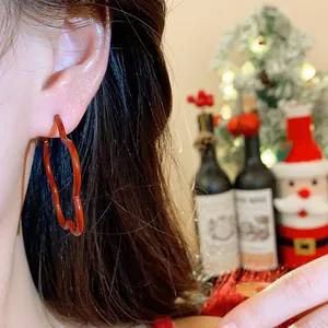 Close-up of red wavy hoop earring worn on an ear with festive background
