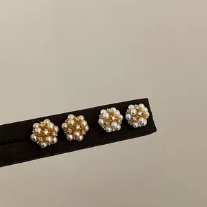 Elegant flower cluster pearl stud earrings with rhinestone detail on a display stand