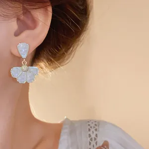 Primo piano di orecchini a fiore in smalto indossati con dettaglio in pizzo bianco.