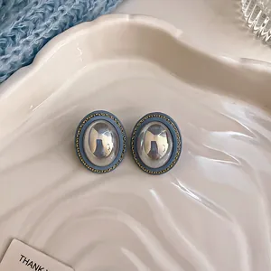 Close-up of vintage blue oval stud earrings with metallic silver center on white plate.
