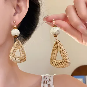 Detail handgefertigter Boho-Rattan-Ohrringe in Dreiecksform mit Holzperlen und Silbernadel.