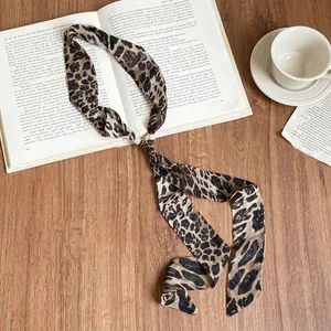 Elegante collana a sciarpa in chiffon leopardato su sfondo di legno con oggetti vintage.