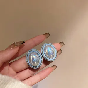 Macro detail of vintage oval stud earrings featuring iridescent center stones and blue enamel borders