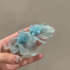 Dettaglio che mostra orecchini a nappa con fiori in tessuto a rete azzurro tenuti in mano