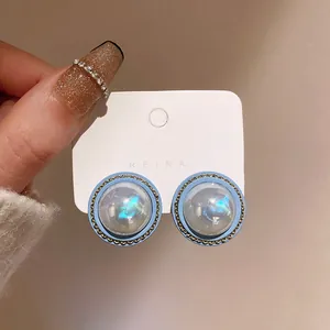 Close-up of retro iridescent pearl stud earrings with blue borders and gold chain trim