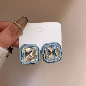 Detailed view of square blue earrings with faceted crystal center and gold chain trim