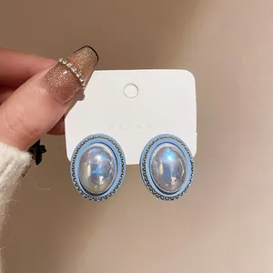 Close-up of vintage blue oval stud earrings with pearl-like luster and gold chain detail.