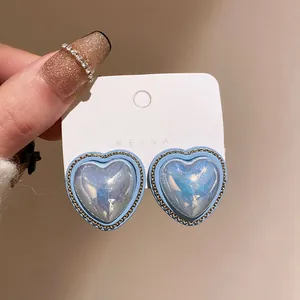 Close-up of blue heart-shaped stud earrings with gold chain border on white card