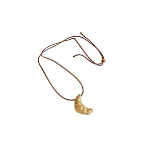 Verstellbare braune Kordelkette mit einem goldfarbenen, texturierten Croissant-Anhänger.