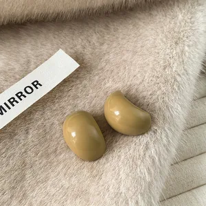Macro detail of curved C-shaped resin stud earrings on a cozy faux fur background.