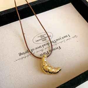Detailansicht eines goldenen Croissant-Anhängers an einer braunen Lederkordel.
