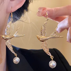 Dettaglio macro di orecchini a rondine dorati vintage con eleganti gocce di perla bianca