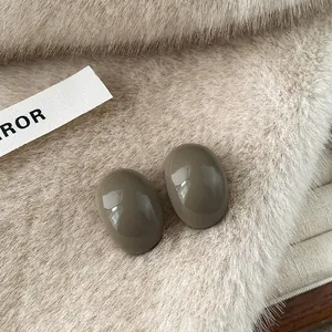 Close-up of glossy oval resin earrings on soft cream-colored faux fur background.