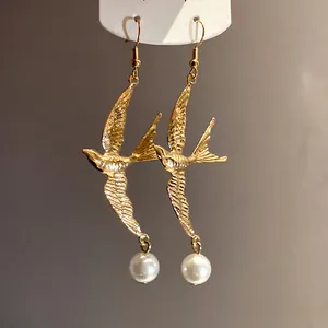 Macro dettaglio di orecchini vintage a forma di rondine dorata con eleganti perle bianche
