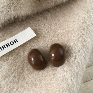 Detail of brown glossy oval resin stud earrings on soft beige fur background